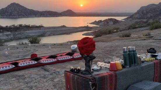 Picnic setup on a rocky outcrop overlooking a river at sunset.