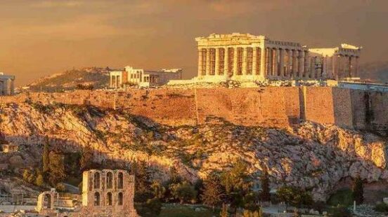 Golden sunlight bathing the Acropolis in Athens, with scattered clouds above.