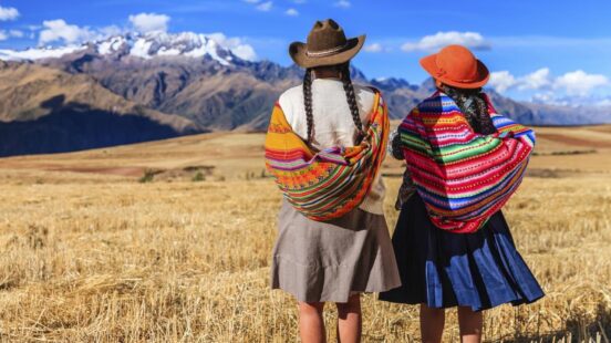 Two people in traditional attire gaze at a mountainous landscape.