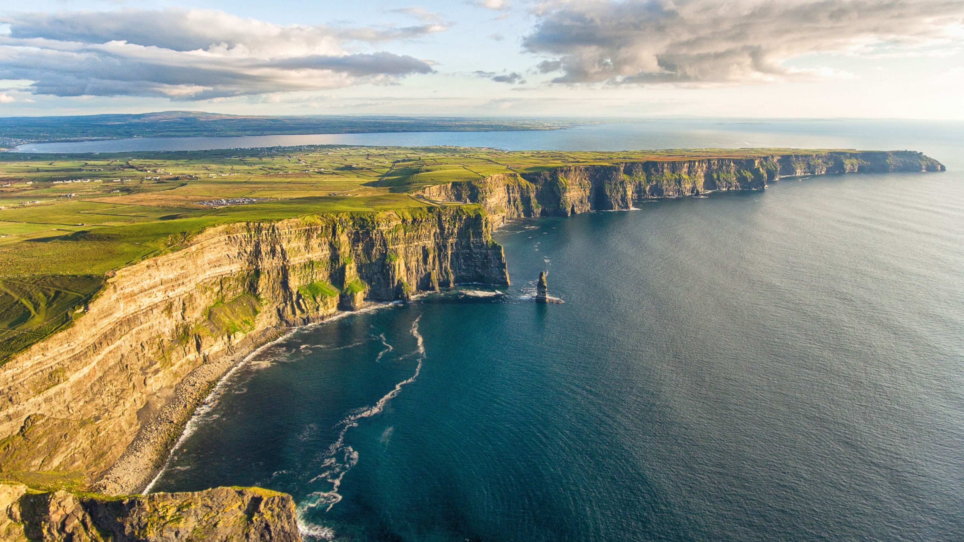 Aerial view of the Cliffs of Moher at sunset with lush greenery and calm sea.