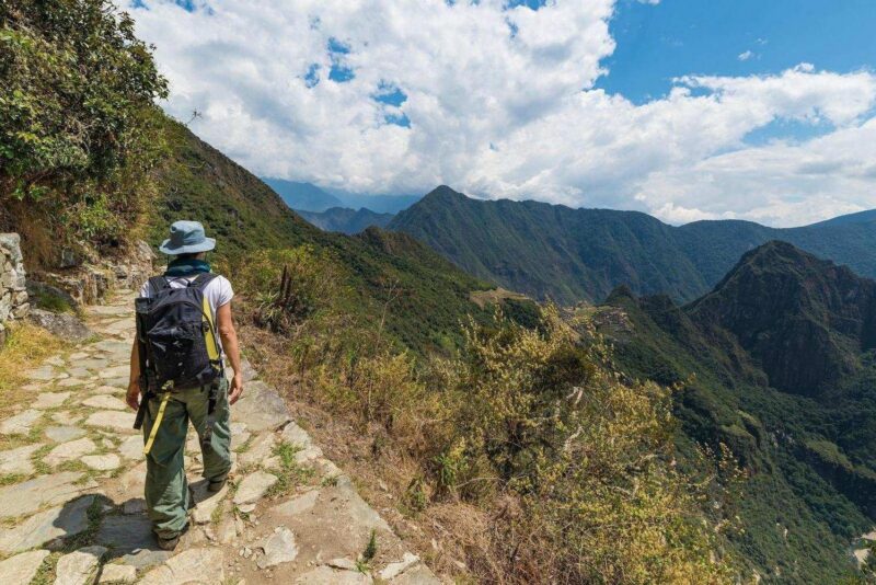 Hiker walking along a stone mountain path overlooking a vast valley during luxury Inca Trail trips.