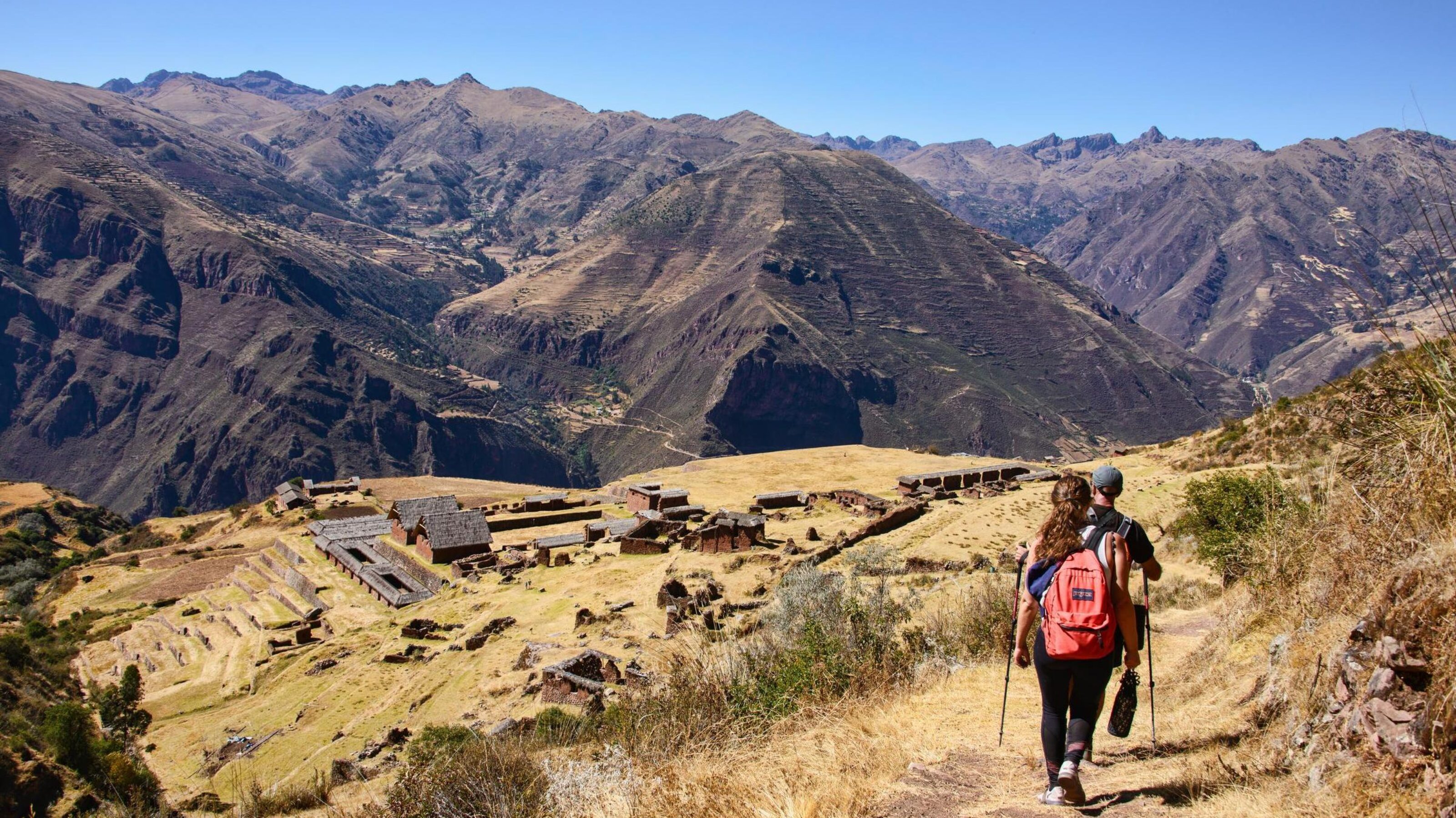 Two hikers descending a hill toward ancient ruins in a mountain valley during luxury Inca Trail trips.