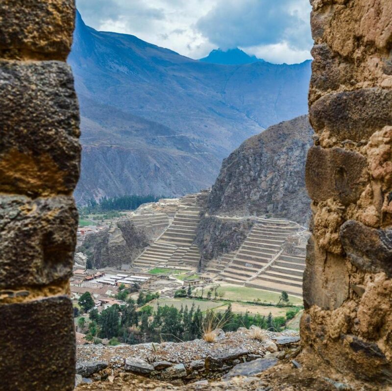View through a stone window of ancient terraces and distant mountains on luxury Inca Trail tours.