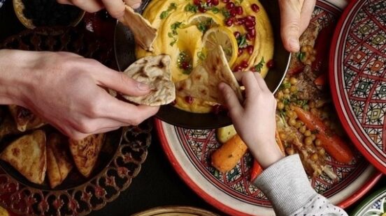 Hands sharing a variety of Middle Eastern dishes on ornate plates.