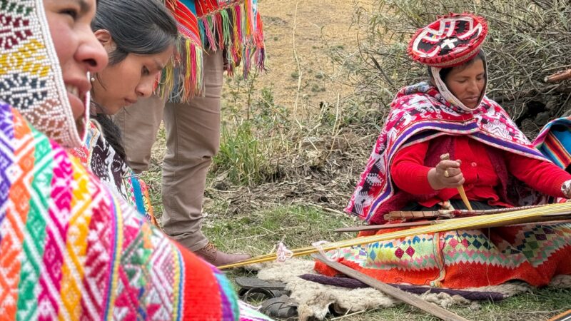 Women in colorful traditional dress weaving textiles during positive impact tours.