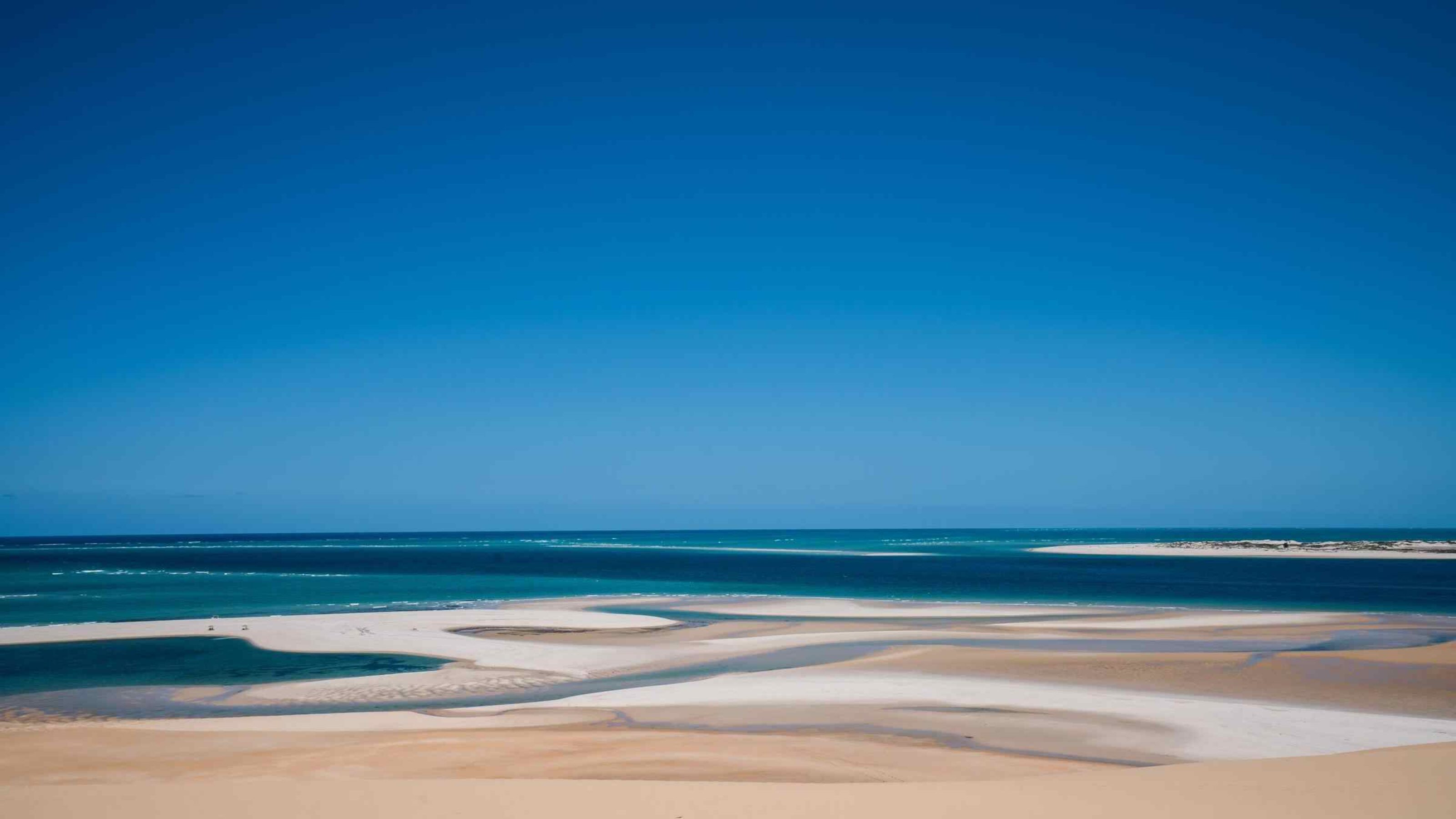 Serene beach with clear blue sky, turquoise water, and sandy shore.