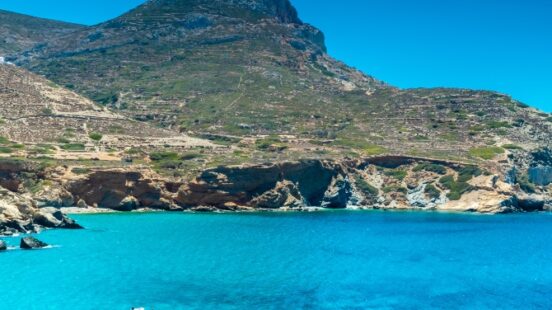 Crystal blue water with a boat in front of a mountainous coastline under a clear sky.