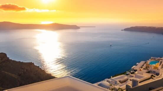 Sunset over a serene sea with white buildings cascading down a cliff.