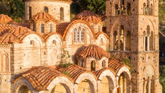 Aerial view of a historic stone monastery with terracotta roofs surrounded by greenery.