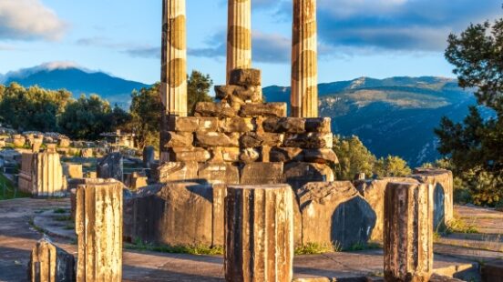 Ancient Greek temple ruins with columns against a mountainous backdrop at sunset.