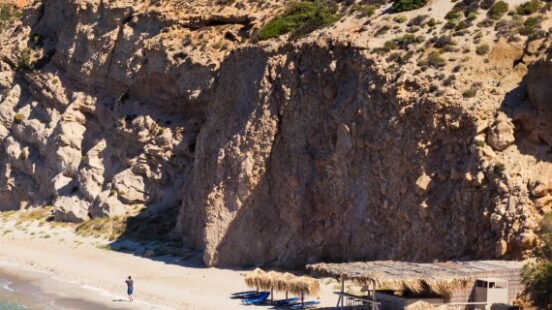 Secluded beach with thatched umbrellas, nestled between rocky cliffs and clear blue waters.