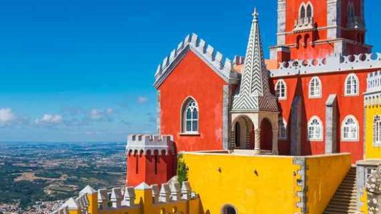 Colourful Pena Palace with red and yellow walls under a blue sky in Sintra, Portugal.