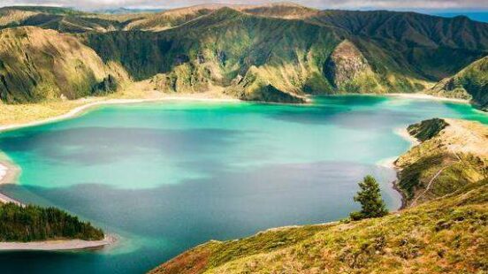 A scenic view of a vibrant blue lake nestled within lush green mountains under a cloudy sky.
