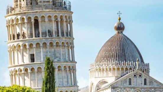 Leaning Tower of Pisa and cathedral against a clear sky with greenery in the foreground.