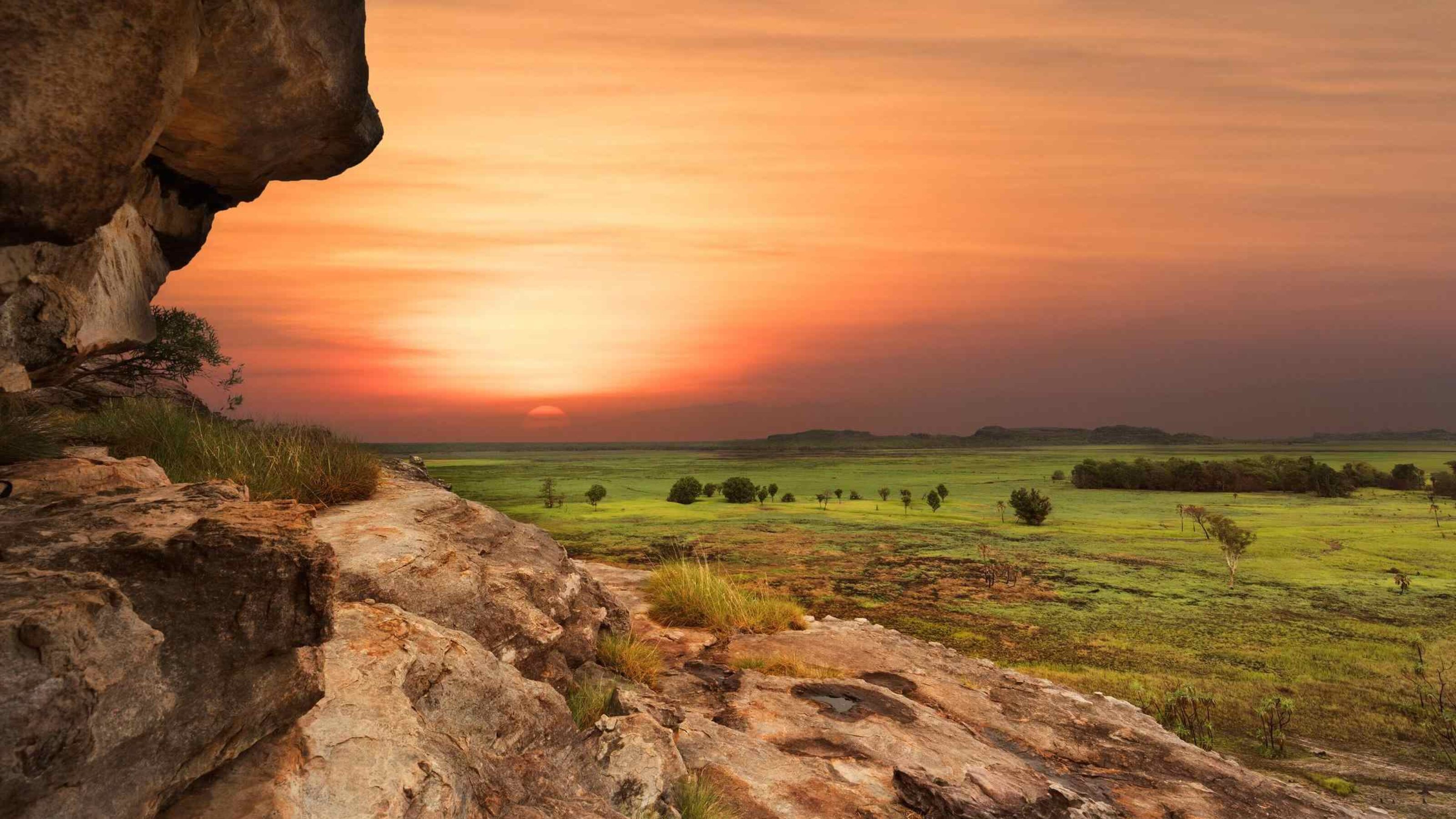 Sunset view over a savanna from behind a rocky outcrop.