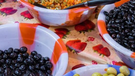 Plastic bowls containing mixed olives with carrots, plain green olives, and black olives at a food stall.
