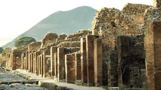 Ancient cobblestone street with ruins and columns leading towards a mountain.