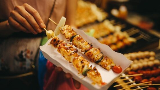 Person holding a plate with three skewers of grilled chicken and vegetables.