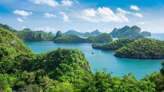 A lush green archipelago with turquoise waters and a boat sailing.
