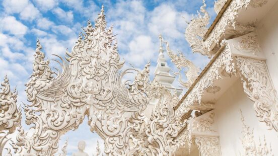 Intricate white temple sculptures beneath a blue sky with clouds.