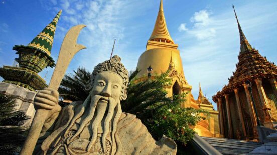 A traditional Thai temple with golden spires and lush greenery under a blue sky.