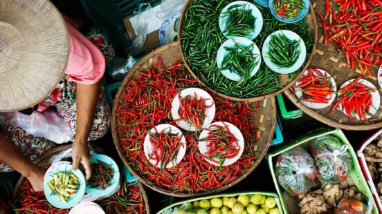 Variety of green and red chilies displayed in bowls and baskets at a market.