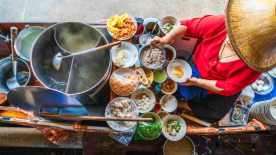 Top-down view of a person preparing food at a vibrant floating market boat stall.