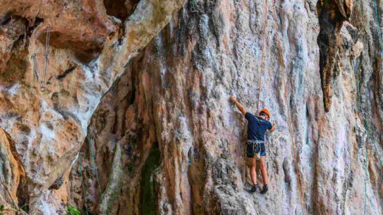 Climber ascending a colorful rocky surface with ropes, wearing a helmet and harness.