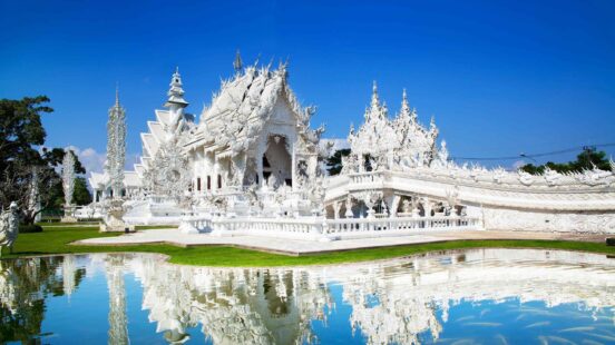 The ornate White Temple in Chiang Rai reflected in a pond with fish.