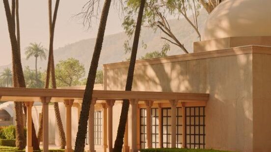 Serene poolside view of a modern building surrounded by tall palm trees and reflective water, under soft, warm sunlight.