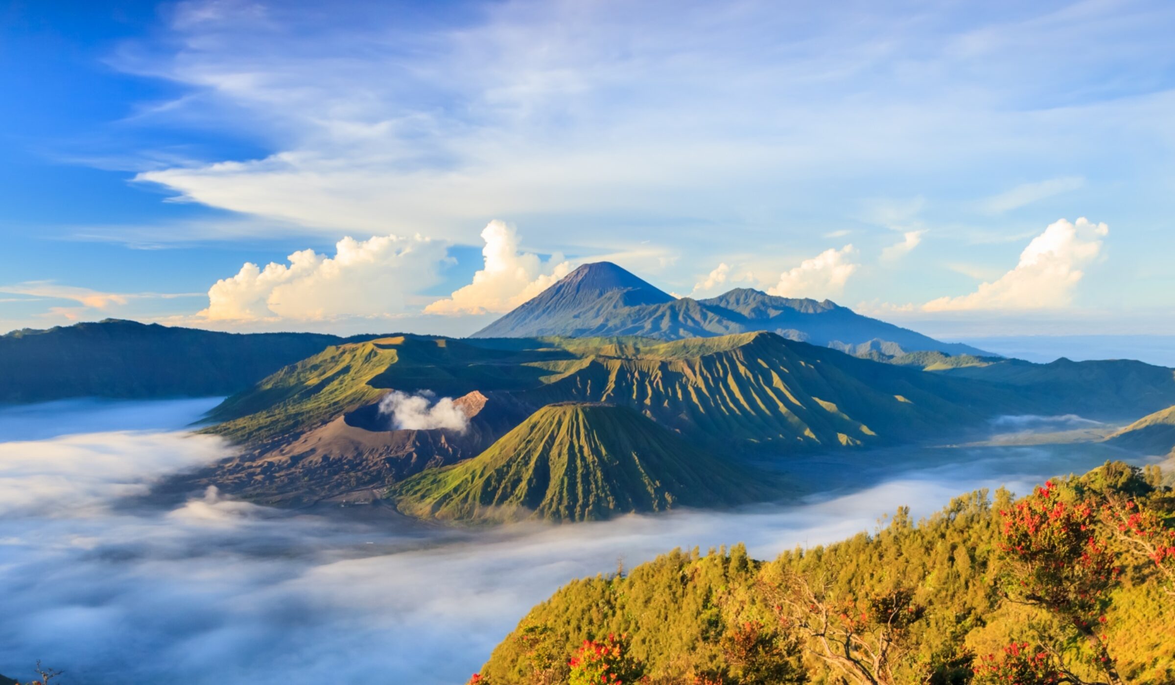 Stunning sunrise over Bromo Tengger Semeru National Park, revealing volcanoes amid dramatic clouds and vibrant green hills.
