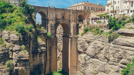 The tall, arched Puente Nuevo bridge spanning a deep gorge in Ronda, Spain, with buildings lining the cliffs on both sides.