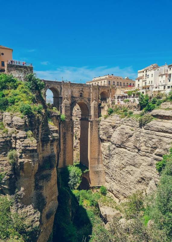 The tall, arched Puente Nuevo bridge spanning a deep gorge in Ronda, Spain, with buildings lining the cliffs on both sides.