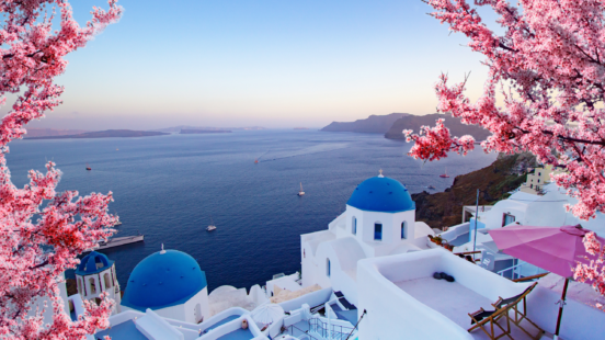 Beautiful View of Oia, Santorini, Greece with Pink Blossoms Flowers at Beautiful Spring Sunset