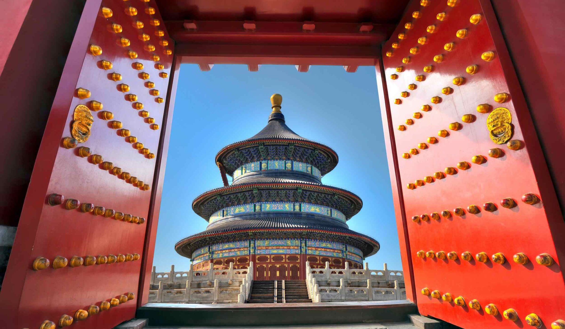View of the Temple of Heaven through open red imperial doors with gold studs during luxury China holidays.