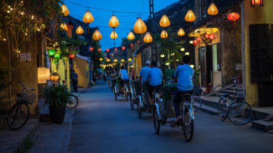 Night view of a street lit by lanterns with people cycling in Hoi An Vietnam