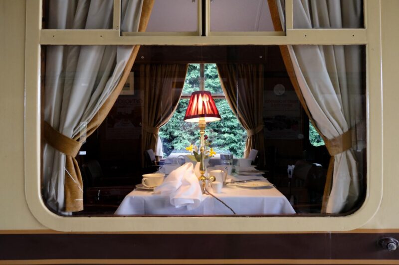 A view into a luxury train dining car through a window, showing a set table with a lamp. Part of luxury Europe rail tours.