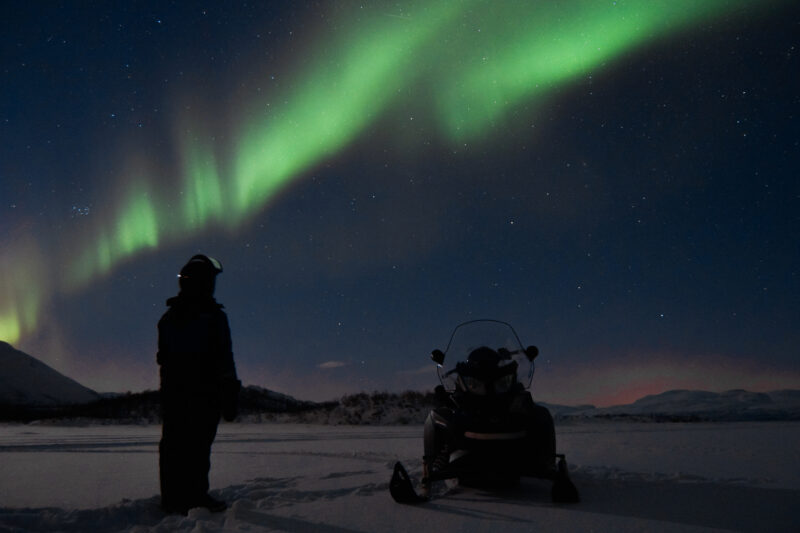 a person stood with a snowmobile watching the northern lights