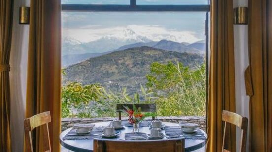 A wooden dining table and blue chairs framing a scenic mountain view through a large window.