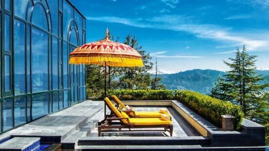 Luxury infinity pool with yellow lounge chairs and a red decorative umbrella overlooking distant mountains.