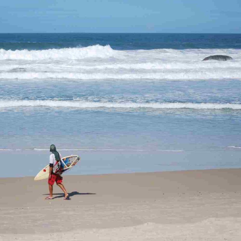 A surfer walks along the beach in Florianópolis
