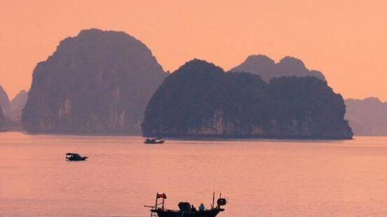 A boat sailing across Ha Long Bay in Vietnam at sunset