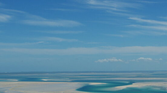 Aerial view of light-colored sandbars and deep turquoise water channels stretching toward a distant horizon.