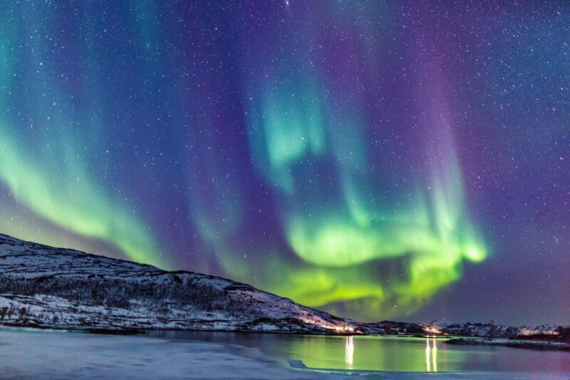 Green and purple northern lights above a mountain and lake landscape