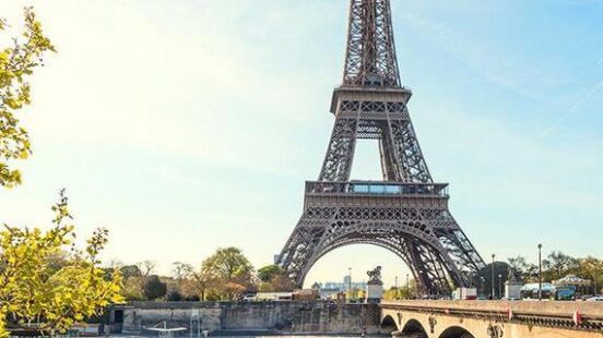View of the Eiffel Tower of Paris across the river, on a sunny day.