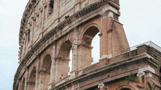 Arched travertine facade of Rome’s Colosseum, framed by olive leaves.
