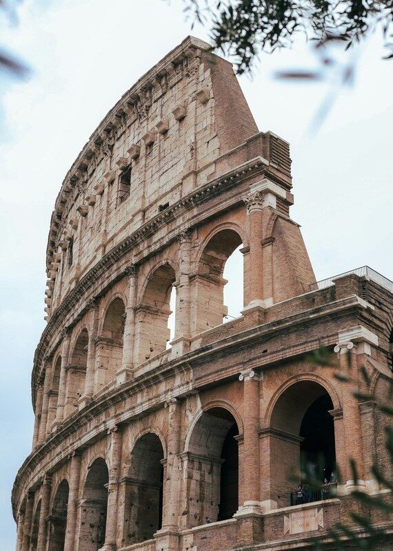 Arched travertine facade of Rome’s Colosseum, framed by olive leaves.