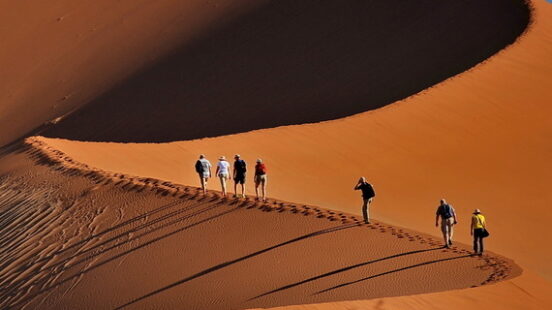 Hikers walking along the ridge of a large desert sand dune on Namibia and Botswana Luxury Safaris.