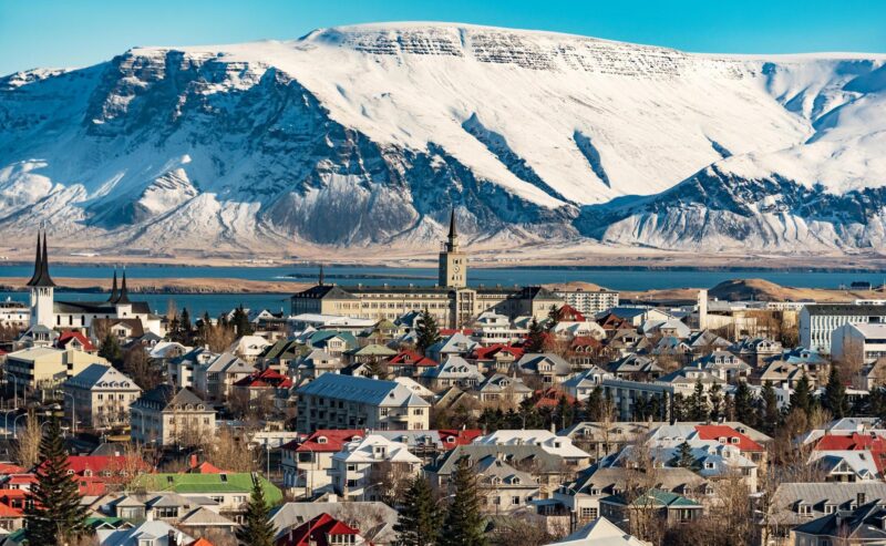 Colorful houses of Reykjavik city in front of a large, snow-capped mountain under a clear blue sky.