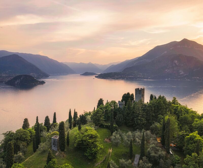 Vertical panoramic aerial view of Vezio Castle with Varenna village and mountains in background during summer sunset. Drone shot in Como lake. Varenna, Italy.